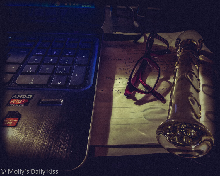 Glass dildo on desk next to glasses